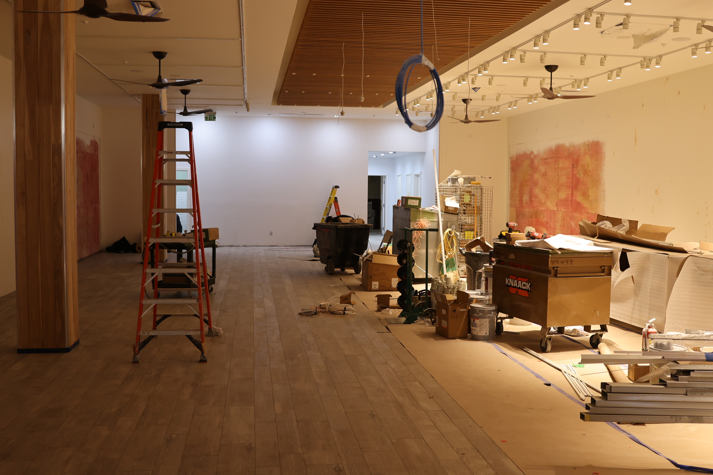 An indoor space under renovation with construction materials from D Barnes Construction, a ladder, and debris scattered around, indicating ongoing work.