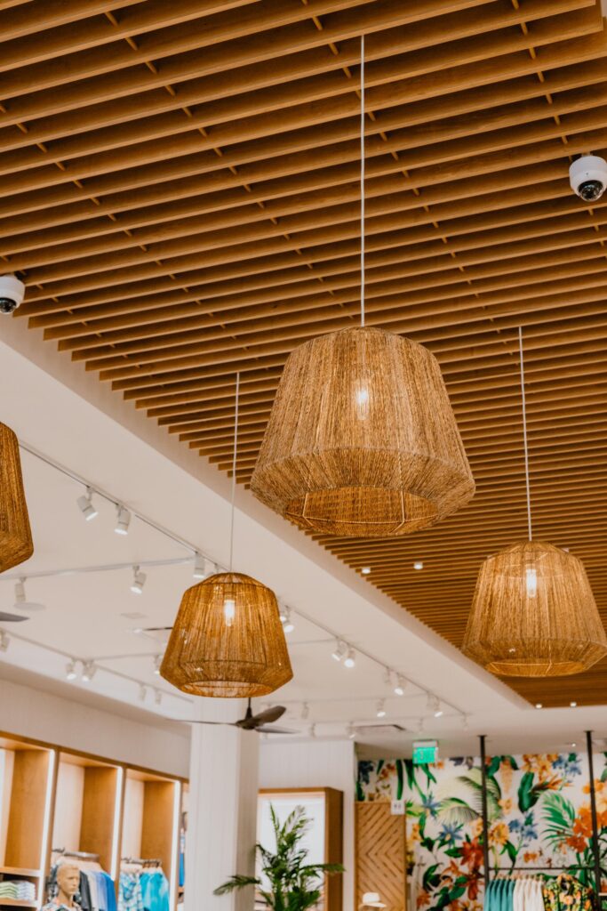 Warmly lit wicker pendant lamps hanging from a modern ceiling with wooden slats, adding a cozy and natural touch to a stylish boutique interior by D Barnes Construction.