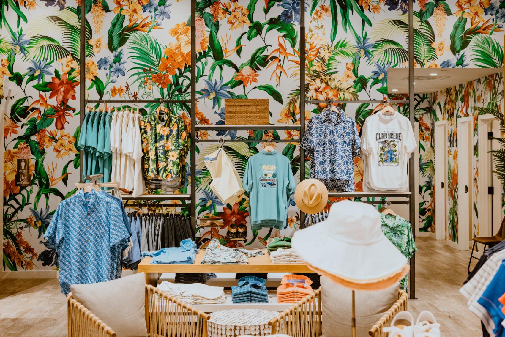 A vibrant tropical-themed clothing store featuring a colorful display of summer apparel and accessories, with lush botanical wallpaper creating an inviting shopping oasis designed by D Barnes Construction.