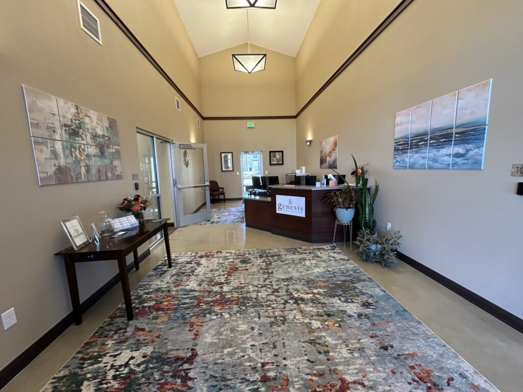 A modern reception area featuring an elegant front desk with the sign "Genesis," decorative plants, a colorful area rug, wall-mounted artwork by D Barnes Construction, providing a welcoming atmosphere.