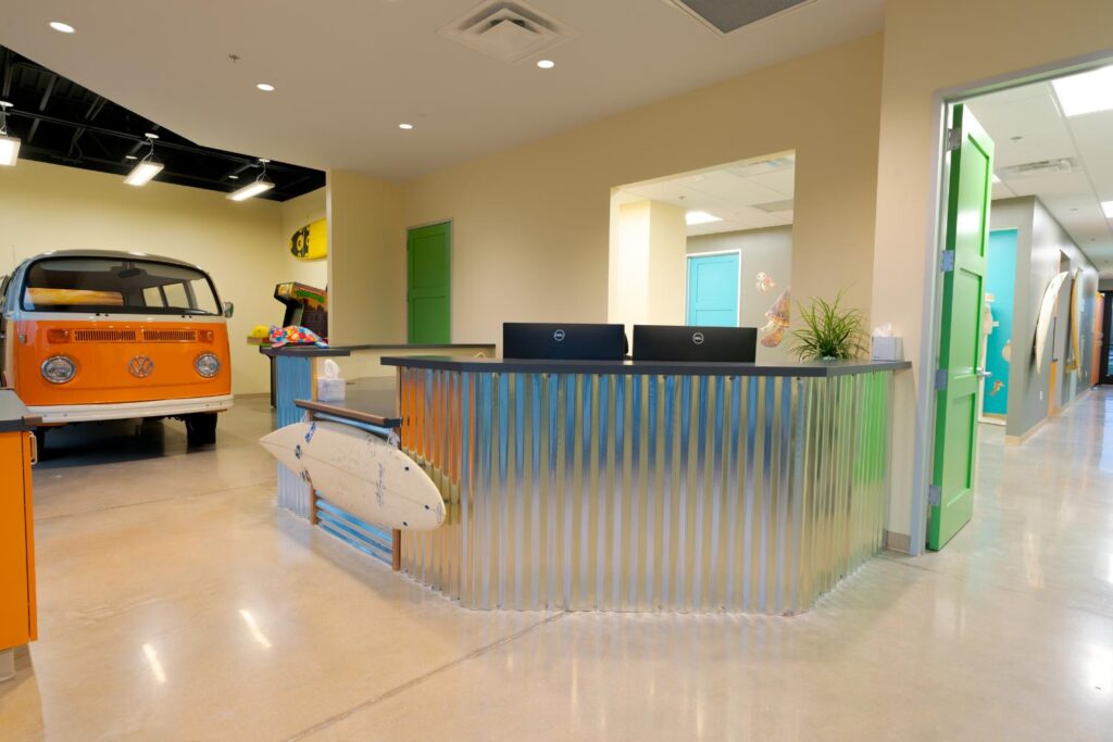 Bright and colorful reception area with a surf-inspired desk design by D Barnes Construction, featuring a vintage orange bus in the corner, adding a playful and nostalgic vibe to the space.